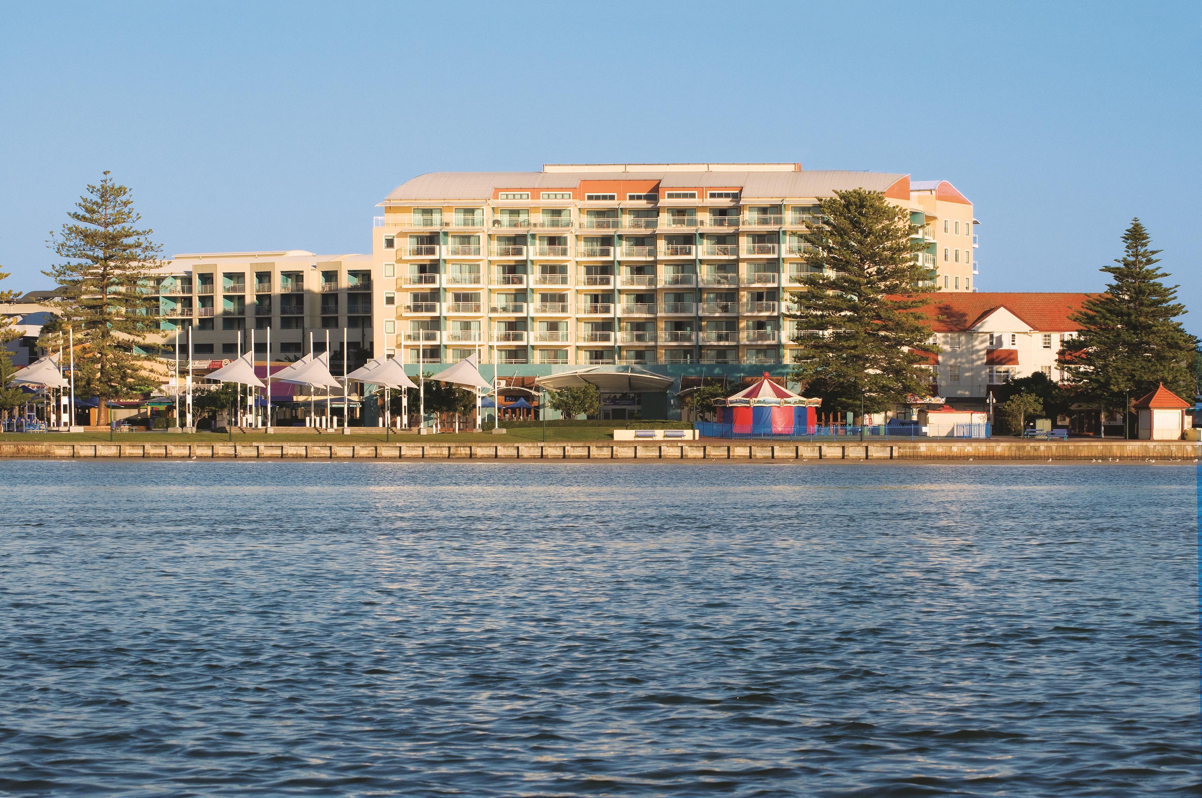 Un hôtel situé au bord de l’eau, avec plusieurs étages, des balcons et un espace piscine.