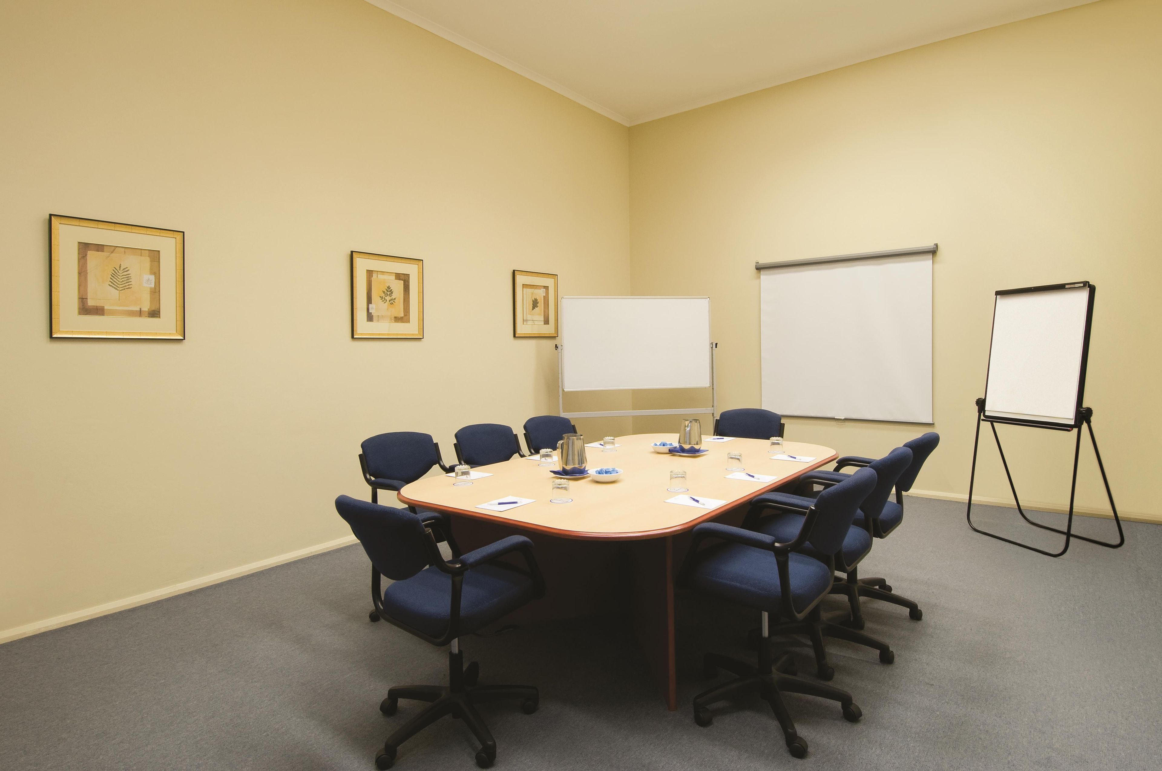Ein Konferenzraum mit einem großen ovalen Tisch, sechs Stühlen, einer Whiteboard-Tafel und drei gerahmten Bildern an der Wand.