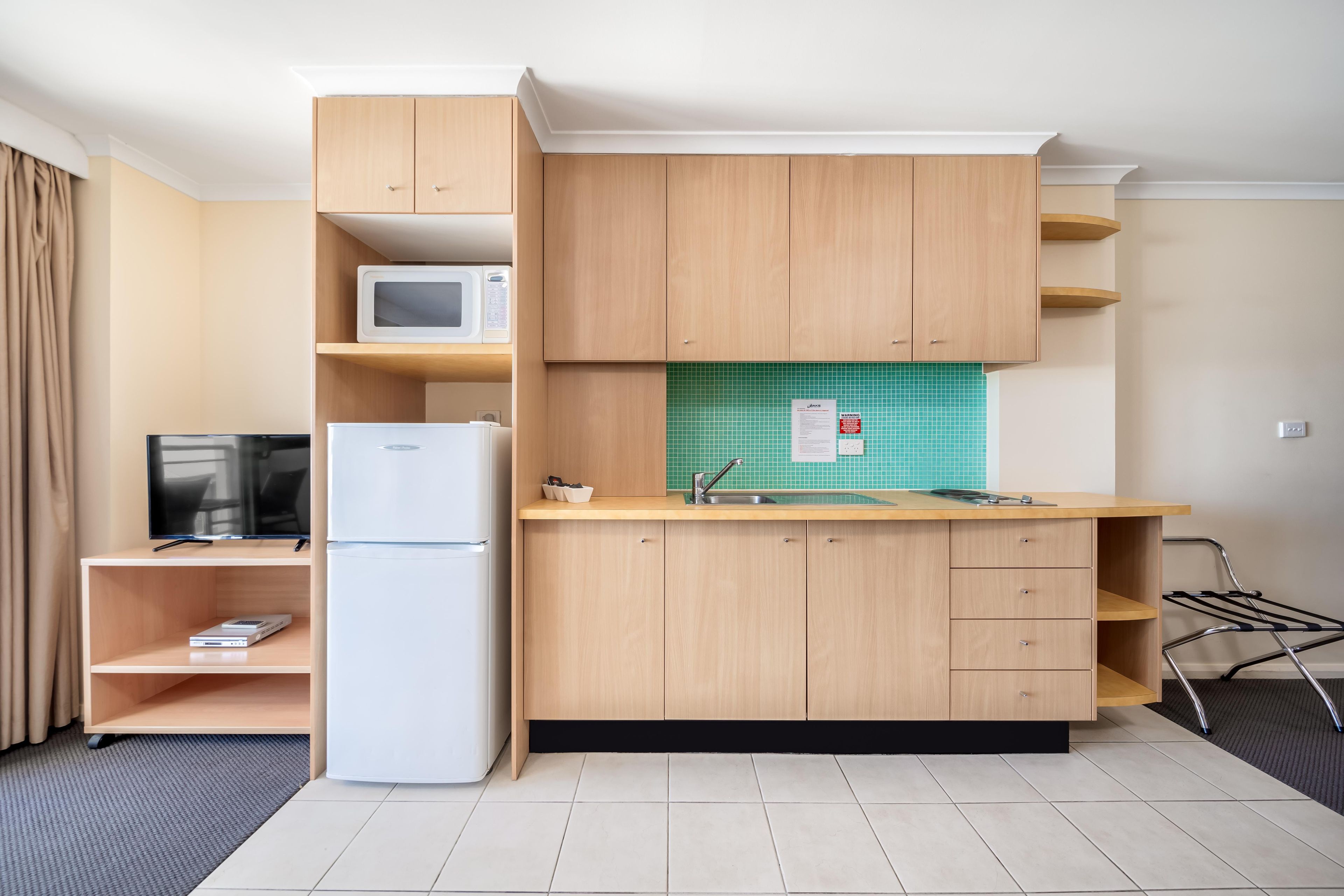 A compact kitchen with a microwave, refrigerator, and a sink with a tiled backsplash.