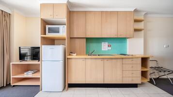 A compact kitchen with a microwave, refrigerator, and a sink with a tiled backsplash.