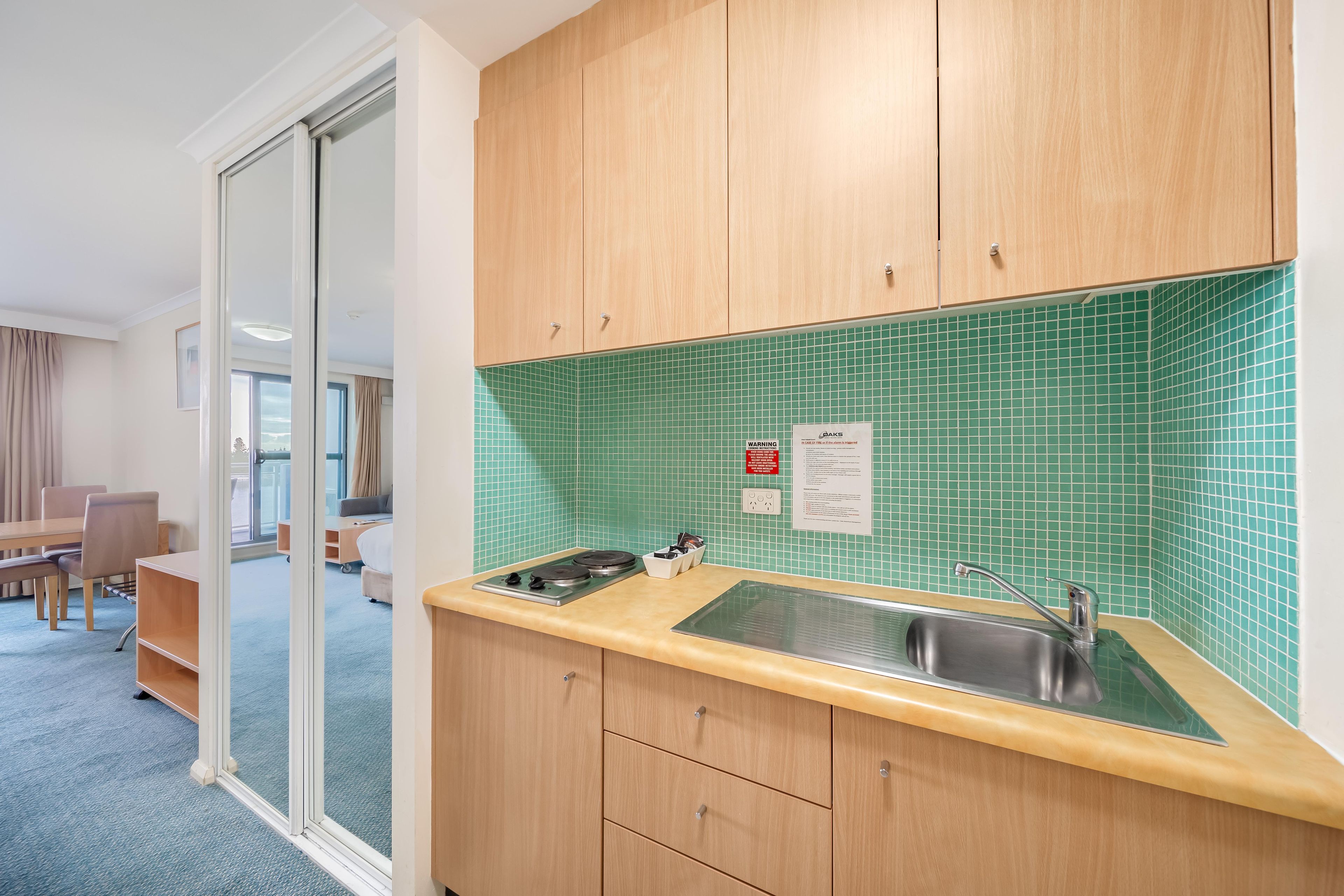 A compact kitchen with a green tiled backsplash, a sink, and a stove.