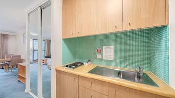 A compact kitchen with a green tiled backsplash, a sink, and a stove.