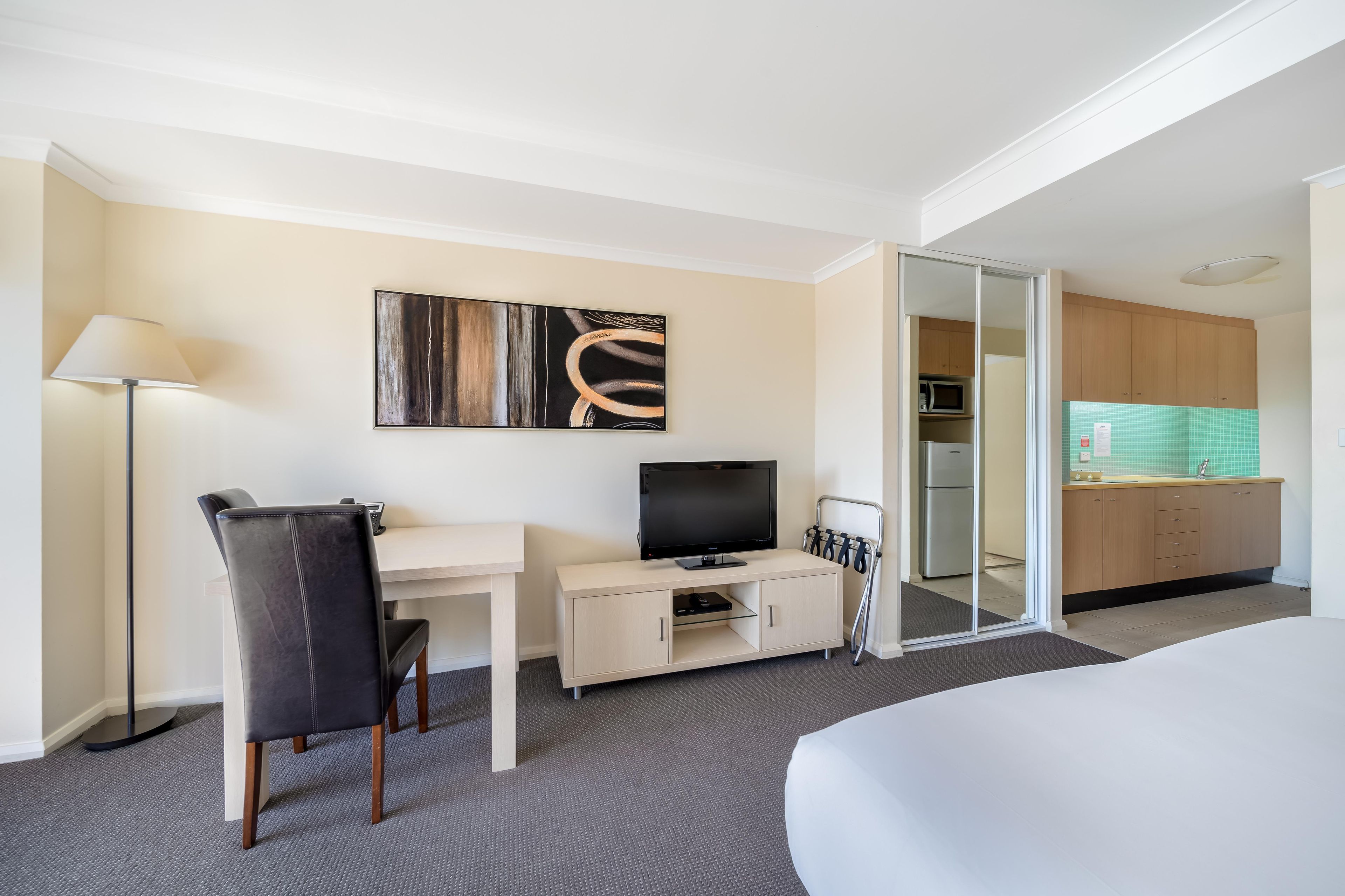 Une chambre d’hôtel comprenant un lit, un bureau avec une chaise, une télévision, un tableau au mur et une kitchenette.