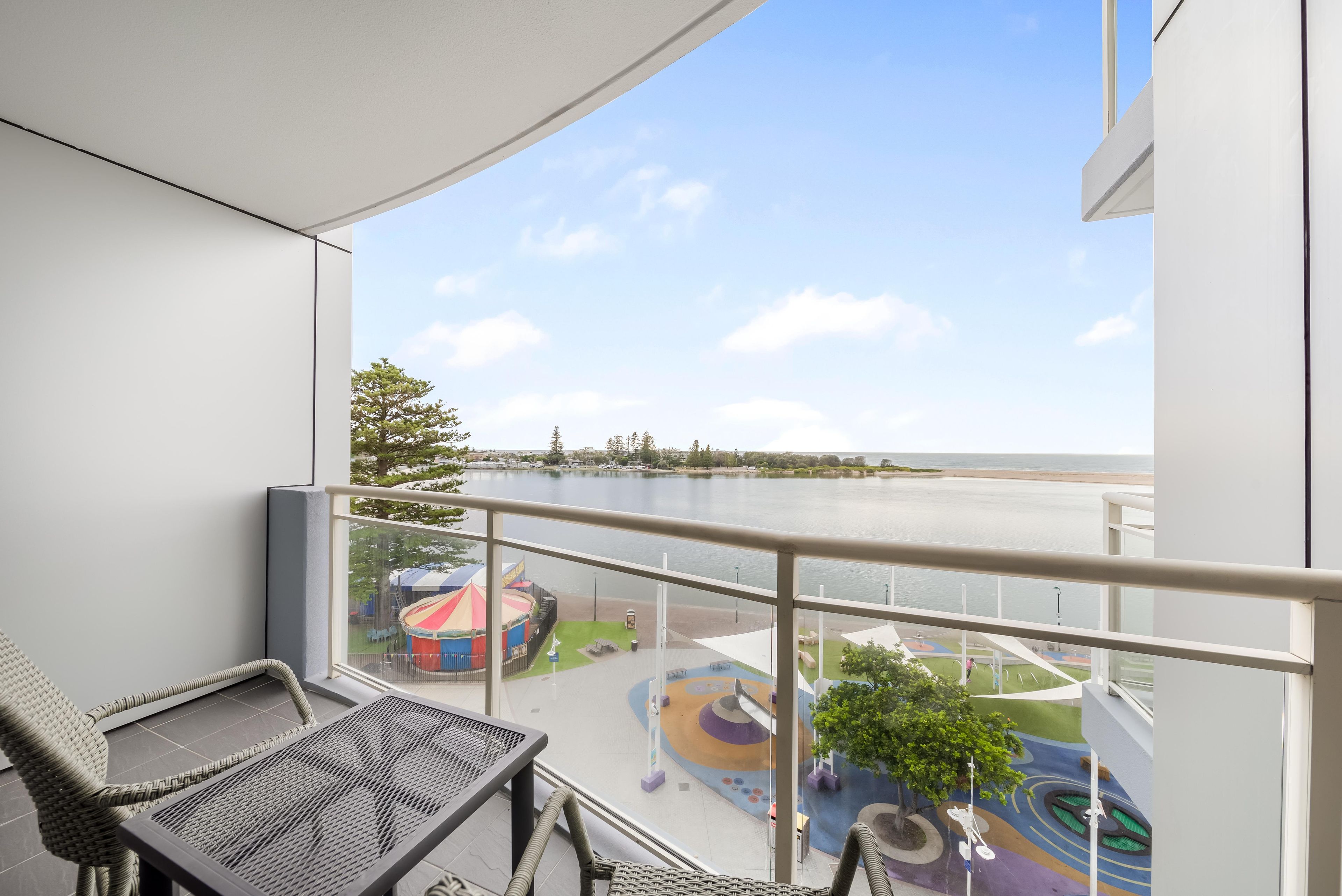 A balcony with a view of a playground and a body of water.