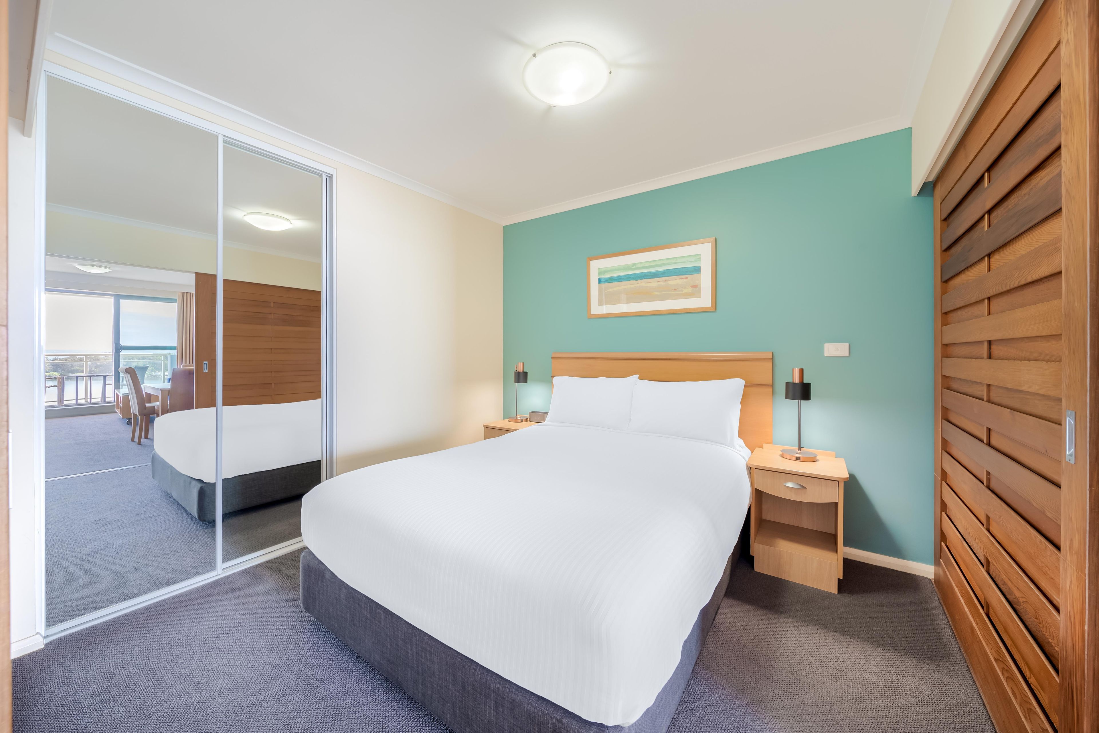 Habitación de hotel con cama, mesitas de noche, escritorio y vistas a través de un ventanal corredero.