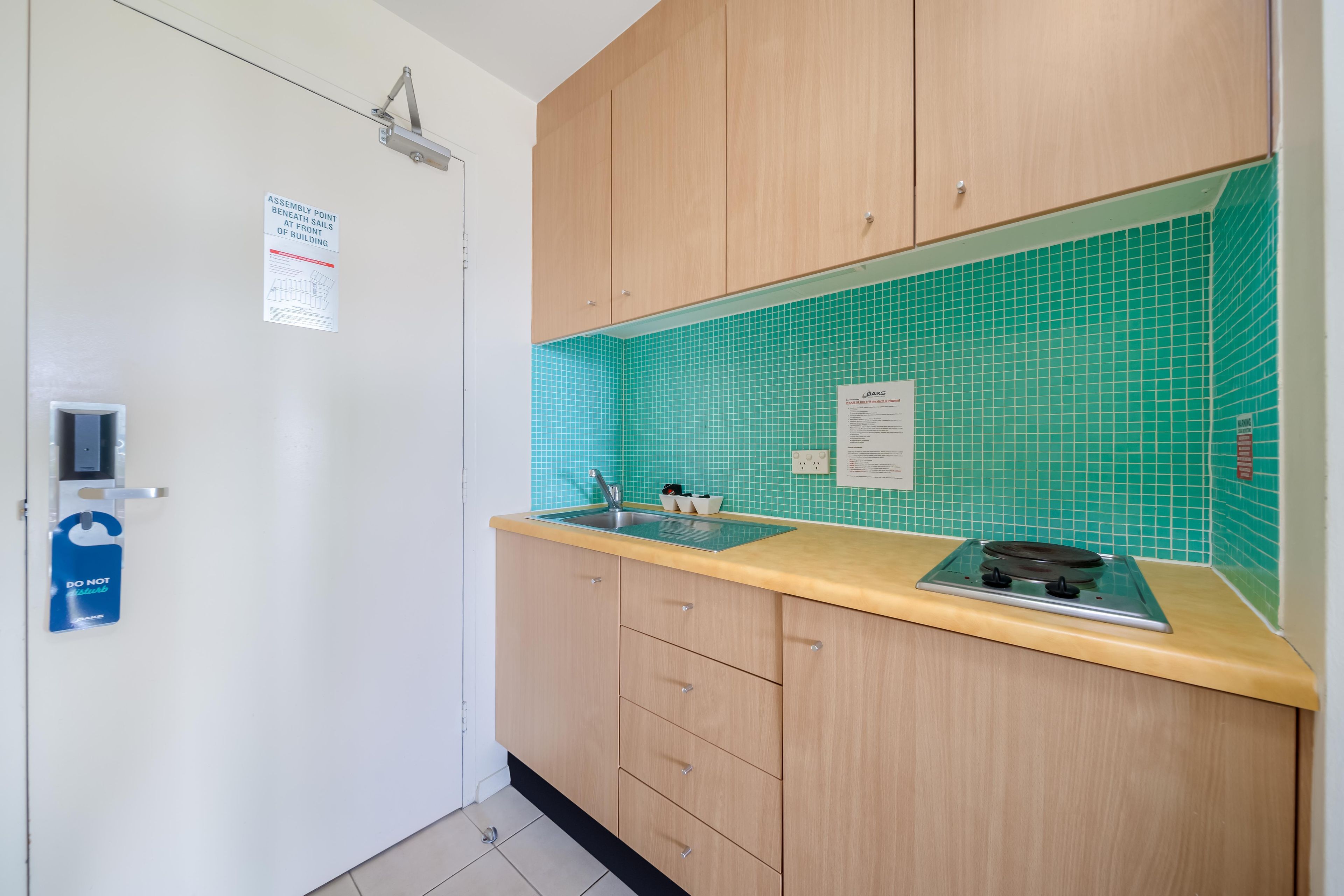 A kitchen with wooden cabinets, a sink, and a stove. There is a sign on the wall and a door with a handle.