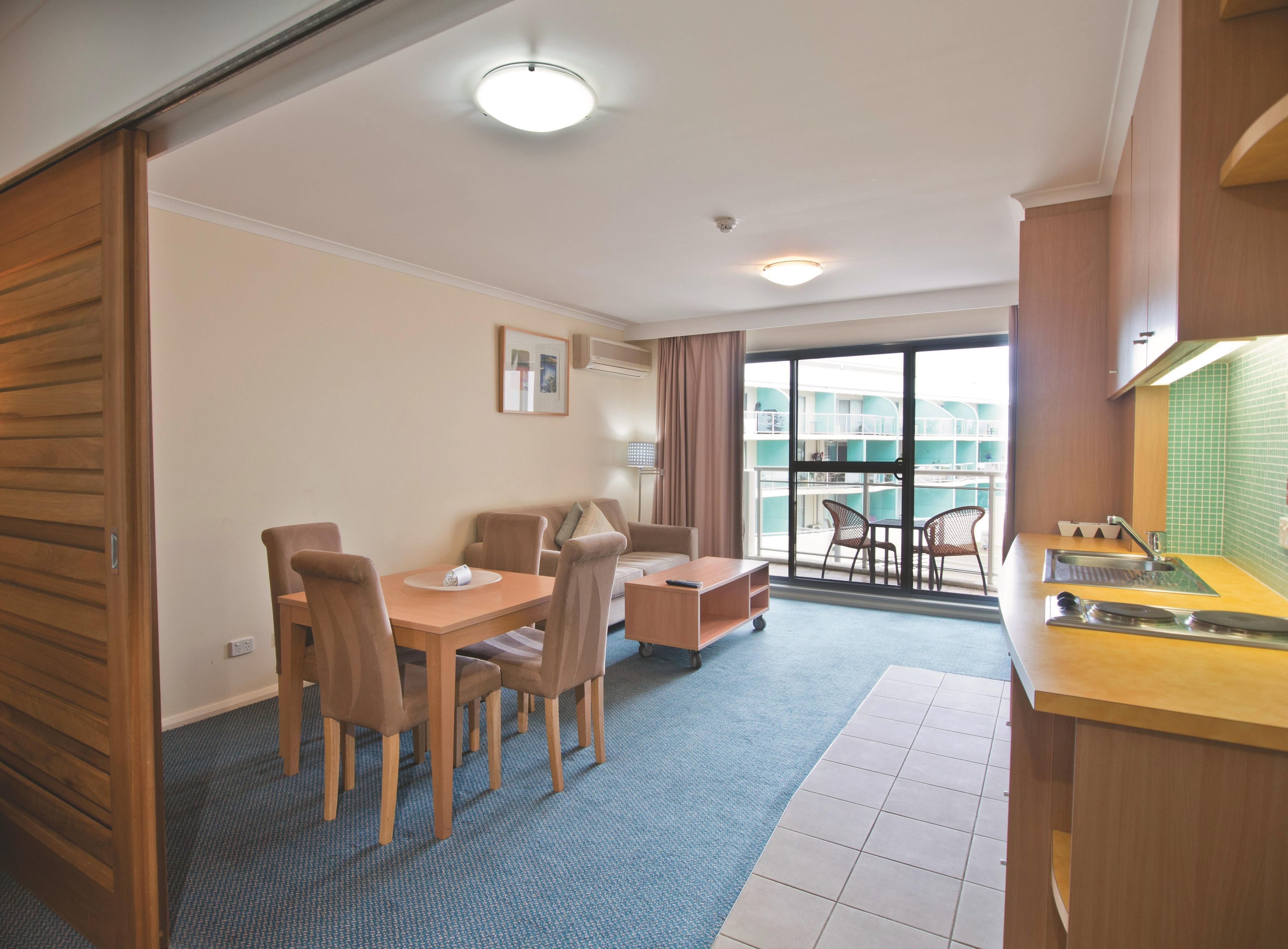 A hotel room with a dining area, kitchenette, and a balcony with a view.