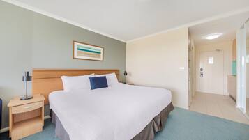 Habitación de hotel con una cama grande, una mesita de noche, una lámpara, un cuadro en la pared y un baño visible a través de una puerta abierta.