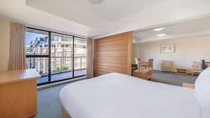 Habitación de hotel con una cama grande, un escritorio, una silla y vistas a la ciudad a través de un ventanal amplio.