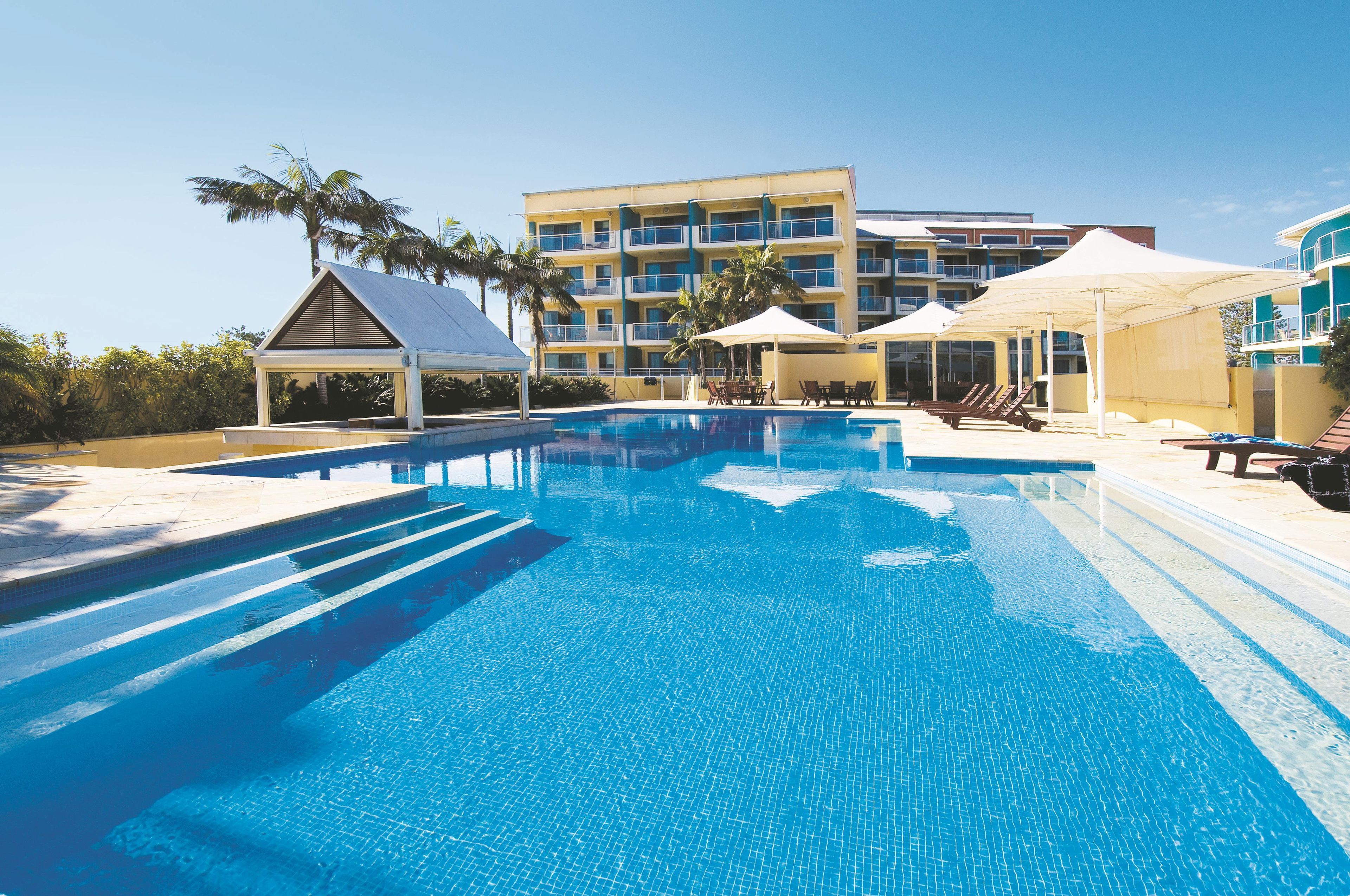 Una piscina al aire libre, sombrillas, sillones reclinables de piscina