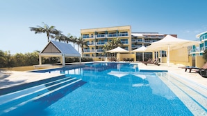 Ein Hotel mit Swimmingpool, Liegestühlen und einer überdachten Sitzgelegenheit.