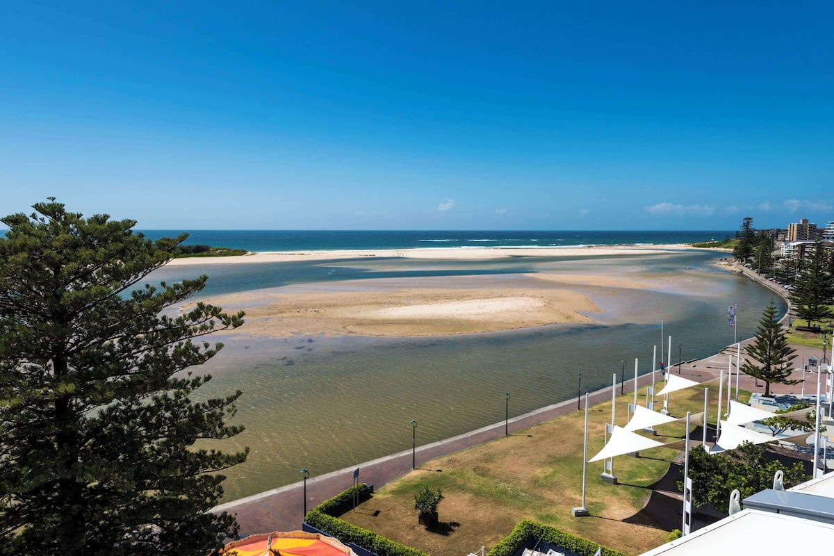 A coastal view with a beach, a clear sky, and a pathway leading to a building with white structures.