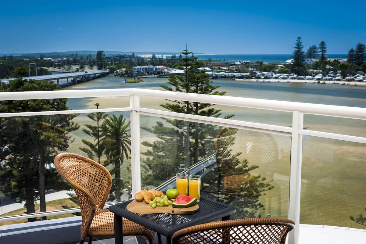 A balcony with a wicker chair, a table with croissants, grapes, watermelon, and orange juice.