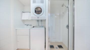A compact laundry room with a front-loading washer and dryer, a glass-enclosed shower, and a small cabinet.