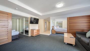 A hotel room with a bed, a desk, a sofa, a TV, and a sliding door leading to a bathroom.