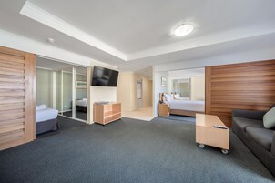 A hotel room with a bed, a desk, a sofa, a TV, and a sliding door leading to a bathroom.