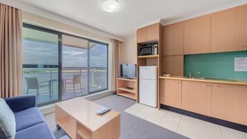 A modern hotel room with a balcony, a sofa, a small table, a television, a microwave, and a refrigerator.