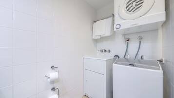 A modern bathroom with a built-in washer and dryer, a toilet, and a towel rack.
