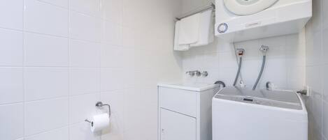A modern bathroom with a built-in washer and dryer, a toilet, and a towel rack.