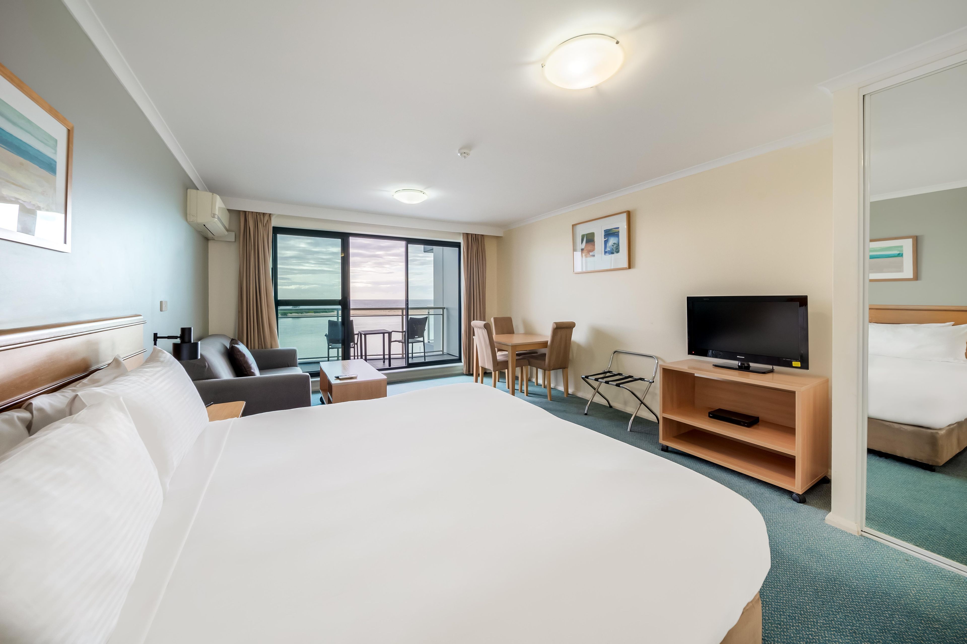 Quarto de hotel com uma cama grande, televisão, escrivaninha e varanda com vista.