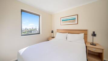 A hotel room with a large bed, a nightstand, a bedside table, a window with a view, and a framed picture on the wall.