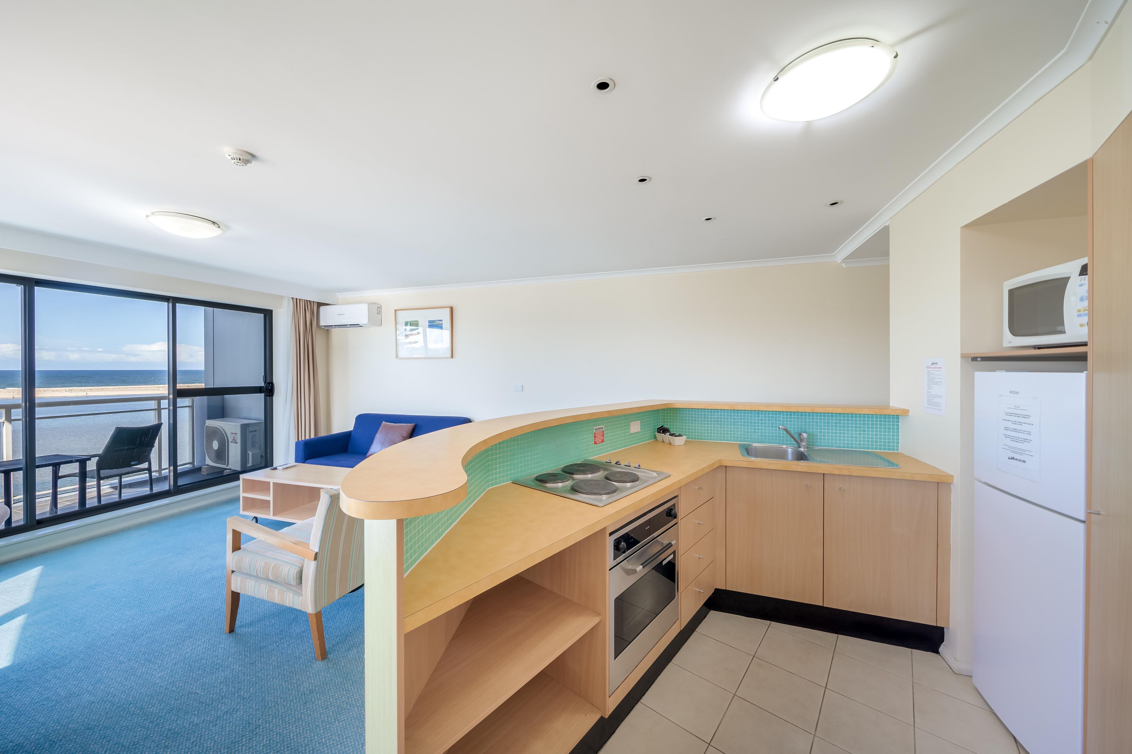 A compact kitchen with a view of the sea, a dining area with a blue sofa, and a small table.