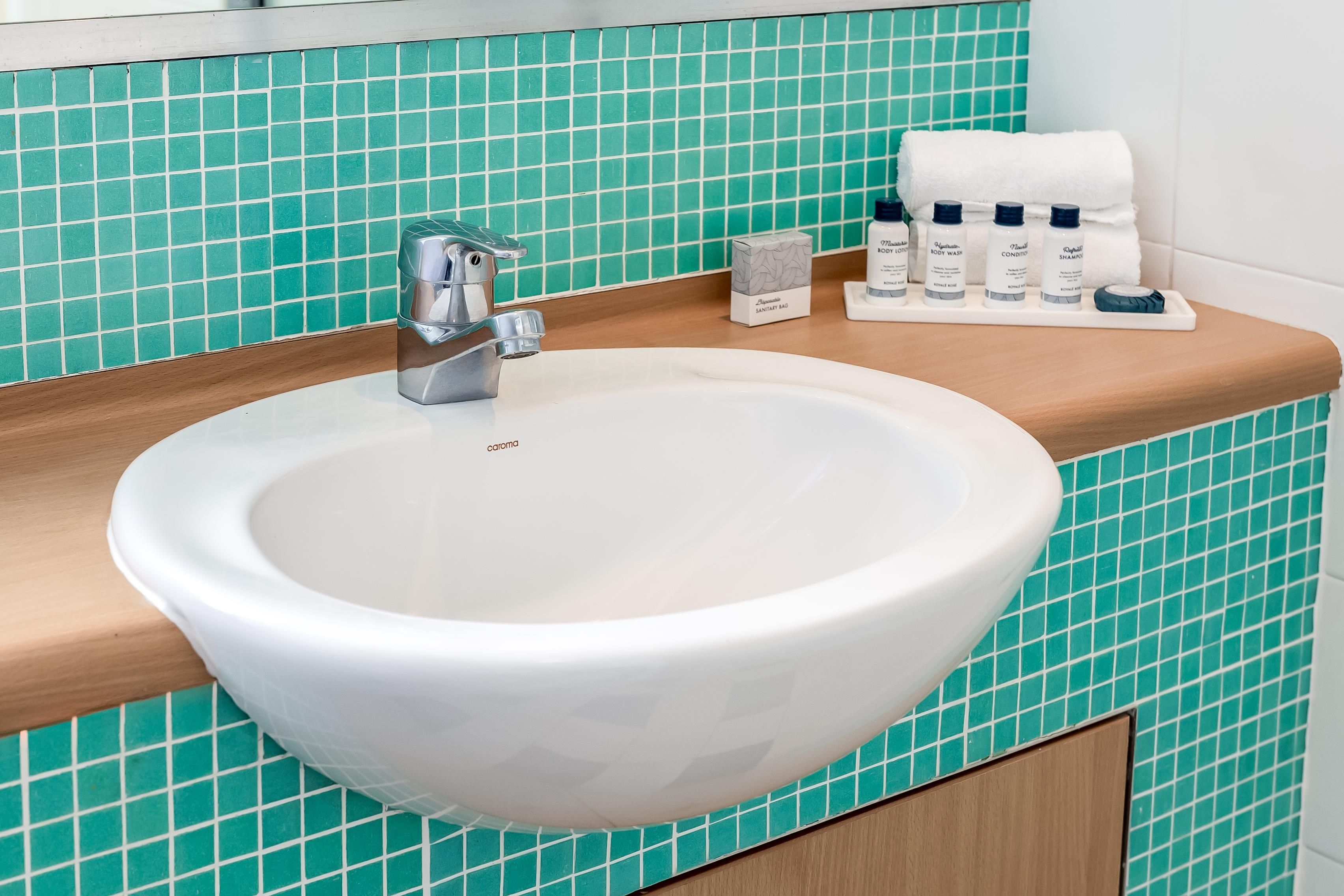 Et badeværelse med en hvid vask, et spejl og en hylde med toiletartikler.