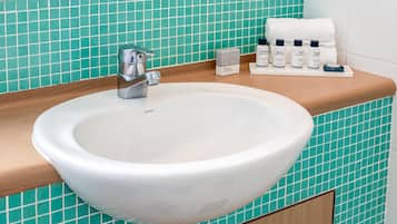Et badeværelse med en hvid vask, et spejl og en hylde med toiletartikler.