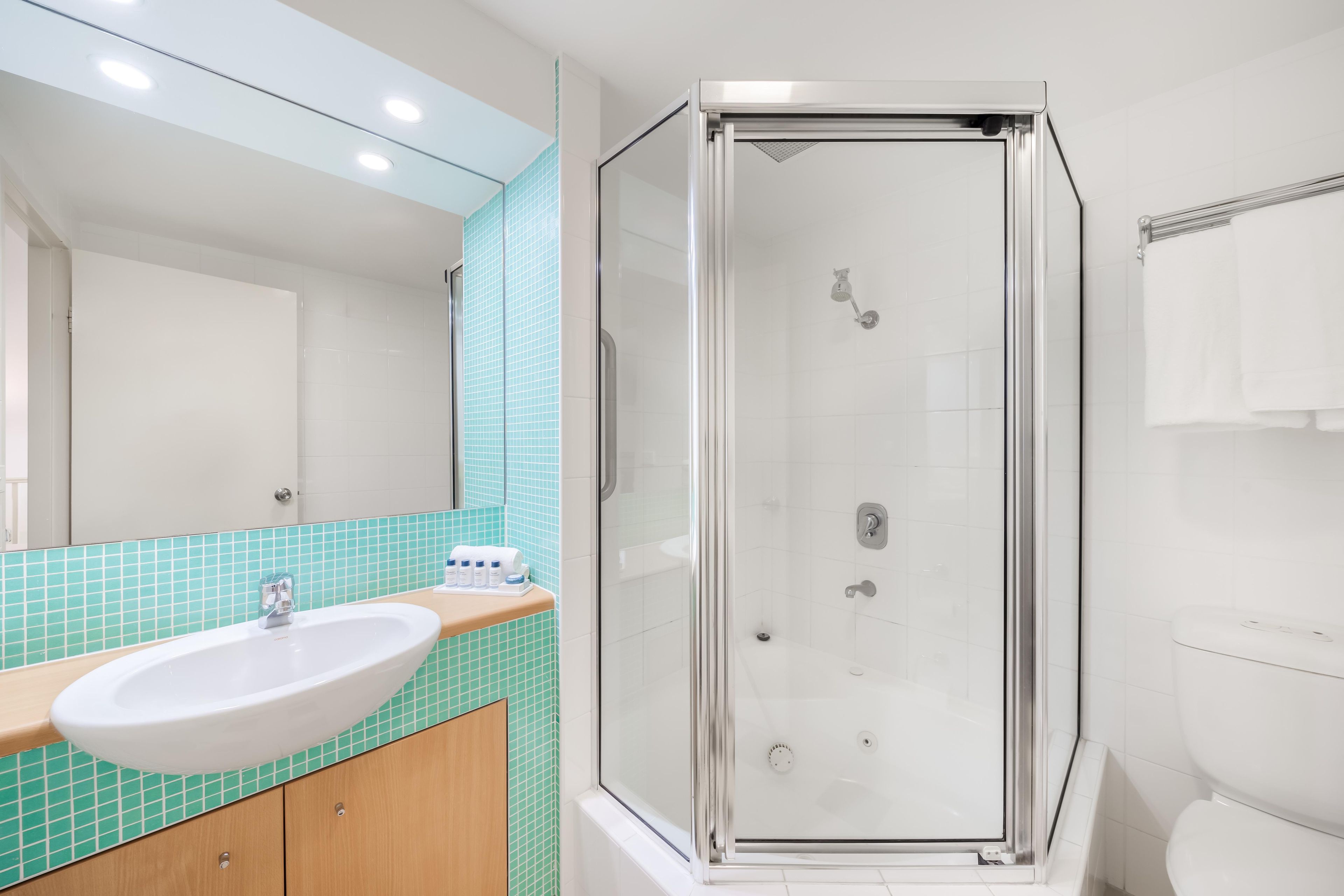 Un baño con lavamanos blanco, espejo, cabina de ducha e inodoro.