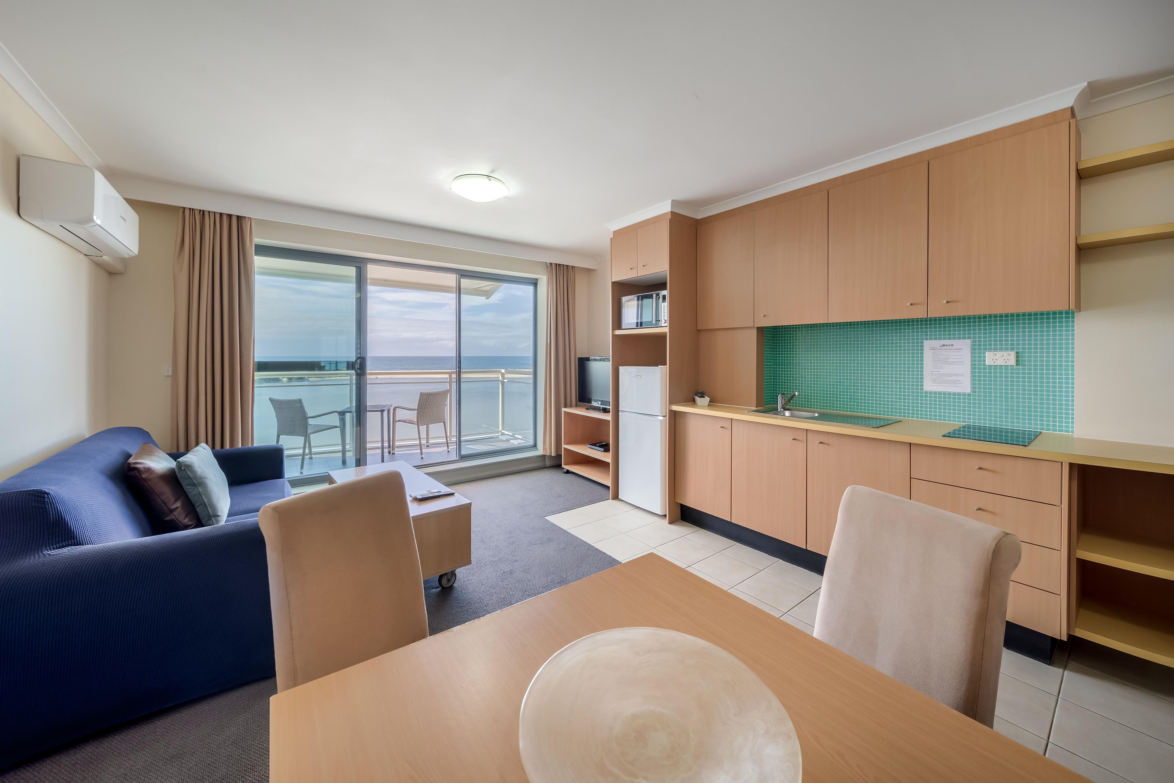 A compact hotel room with a balcony, a kitchenette, a dining area, and a sofa.