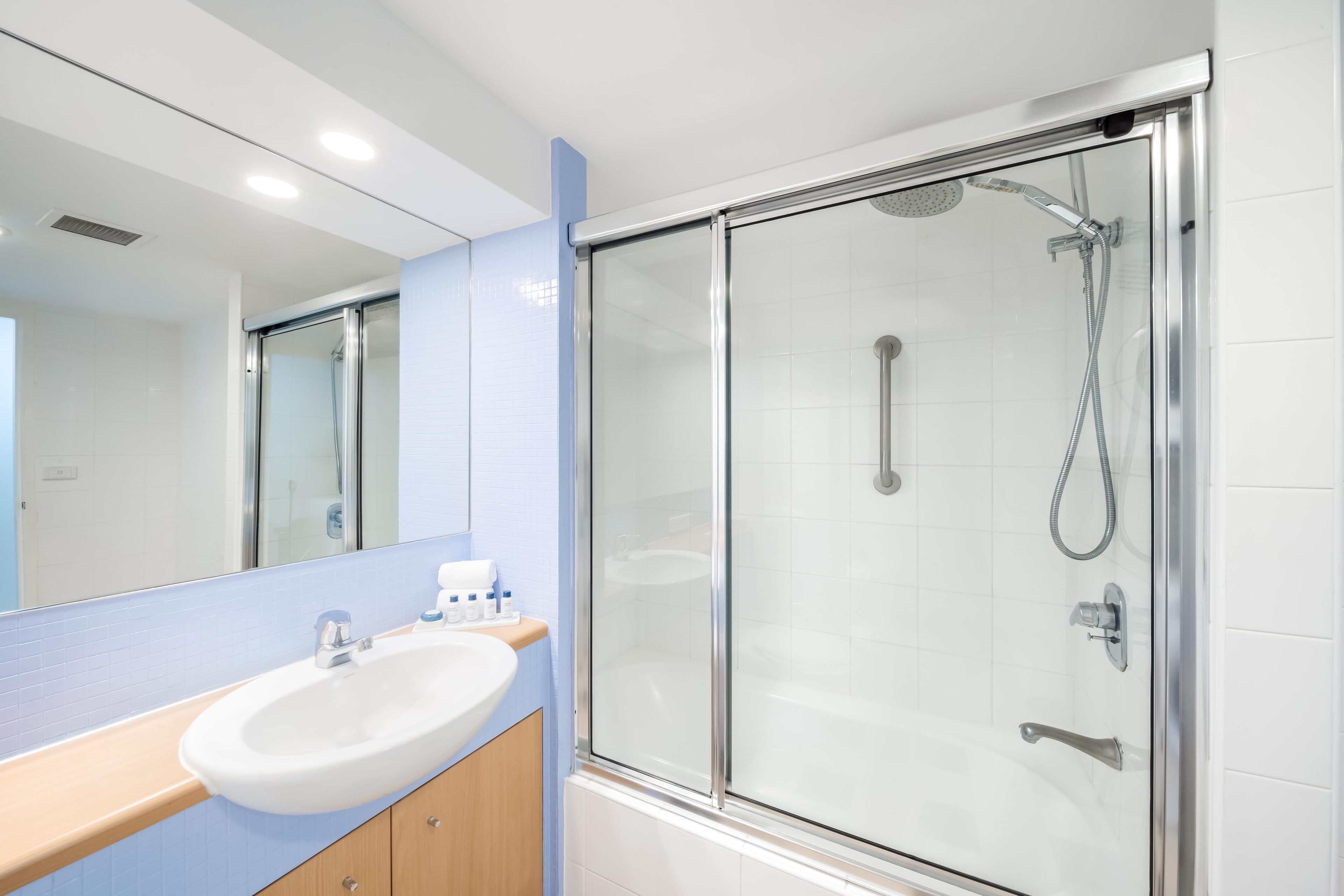 Un baño moderno con ducha de vidrio, lavamanos blanco y espejo.