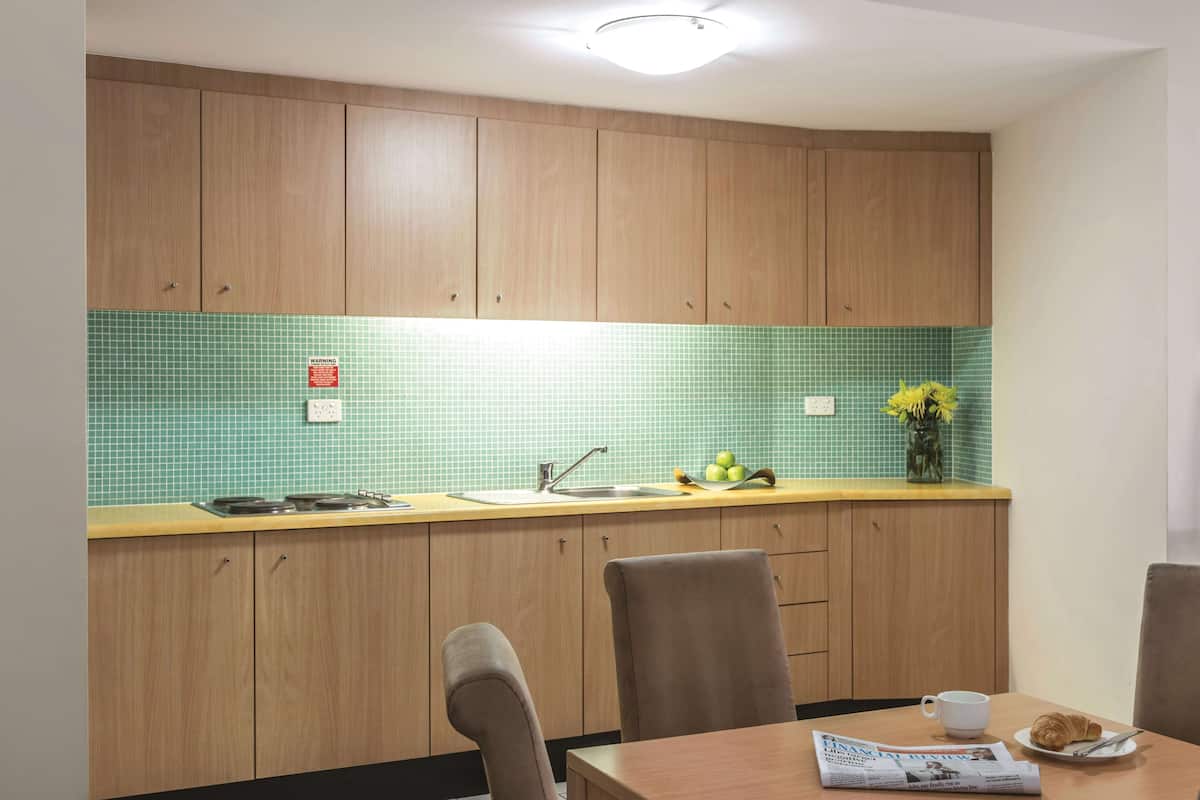 A kitchen with wooden cabinets, a green tiled backsplash, a sink, and a dining area with chairs and a table.
