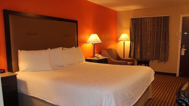 A hotel room with a large bed, two bedside lamps, a chair, and a desk with a telephone.
