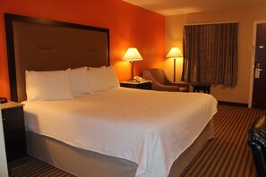 Ein Hotelzimmer mit einem großen Bett, zwei Nachttischlampen, einem Sessel und einem Schreibtisch mit Telefon.