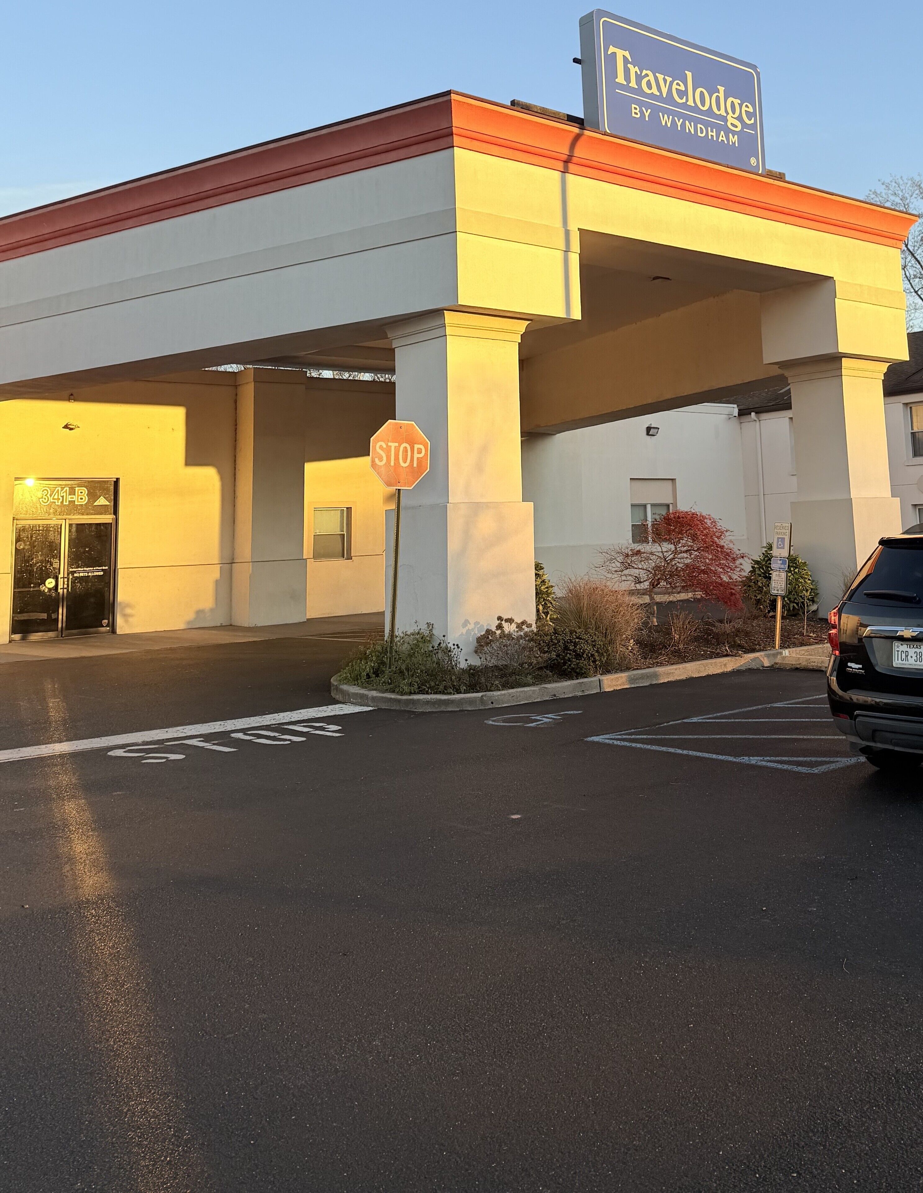 A Travelodge by Wyndham hotel with a stop sign, parking spaces, and a clear sky.