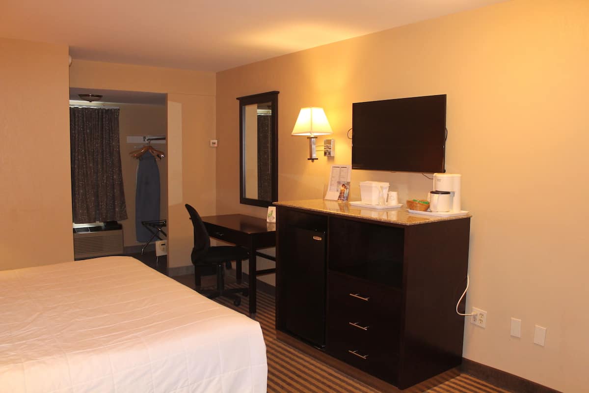 A hotel room with a bed, a desk with a lamp, a television, and a coffee maker.