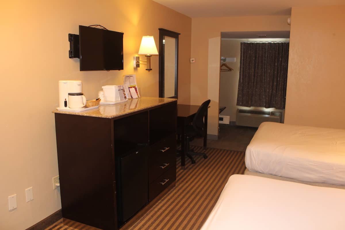A hotel room with a bed, a desk with a coffee maker, a chair, a mirror, and a shower area.