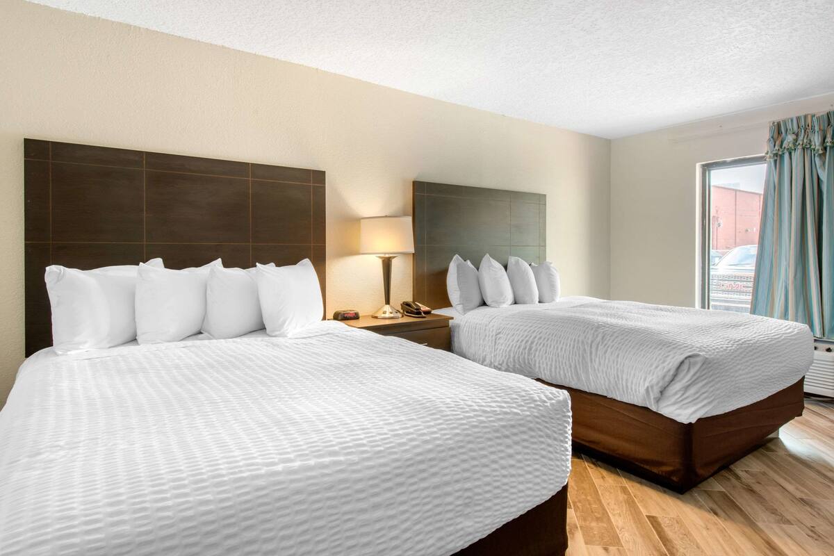 A hotel room with two beds, a nightstand with a lamp, and a window with curtains.