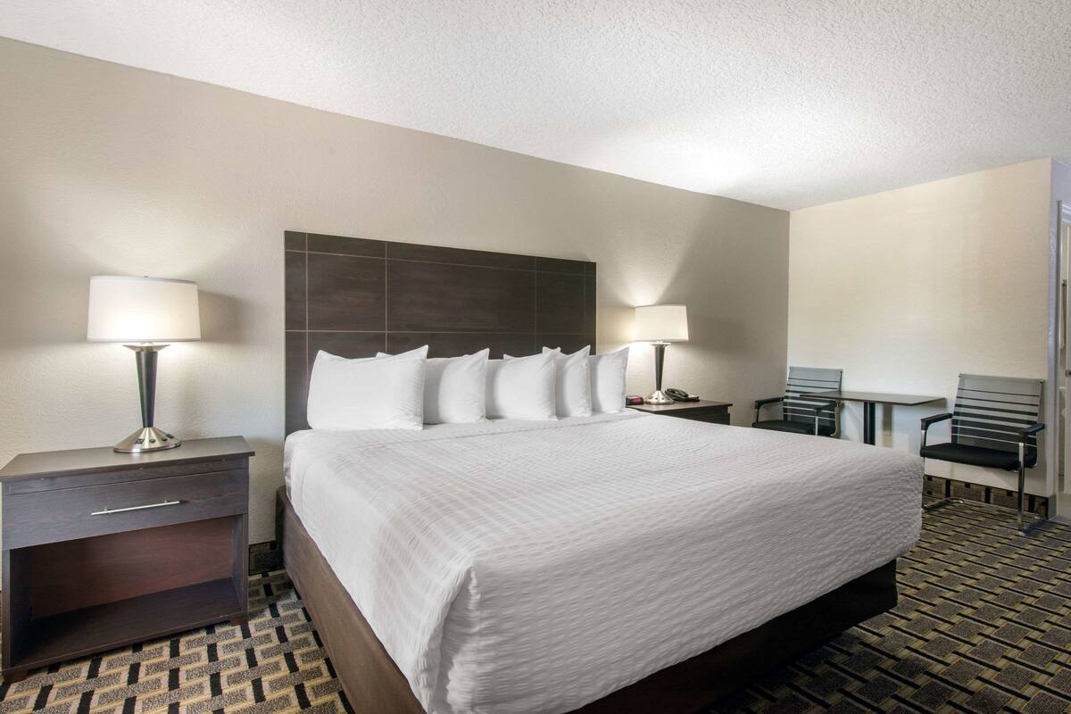 A hotel room with a large bed, two bedside tables with lamps, a small desk with a chair, and a patterned carpet.