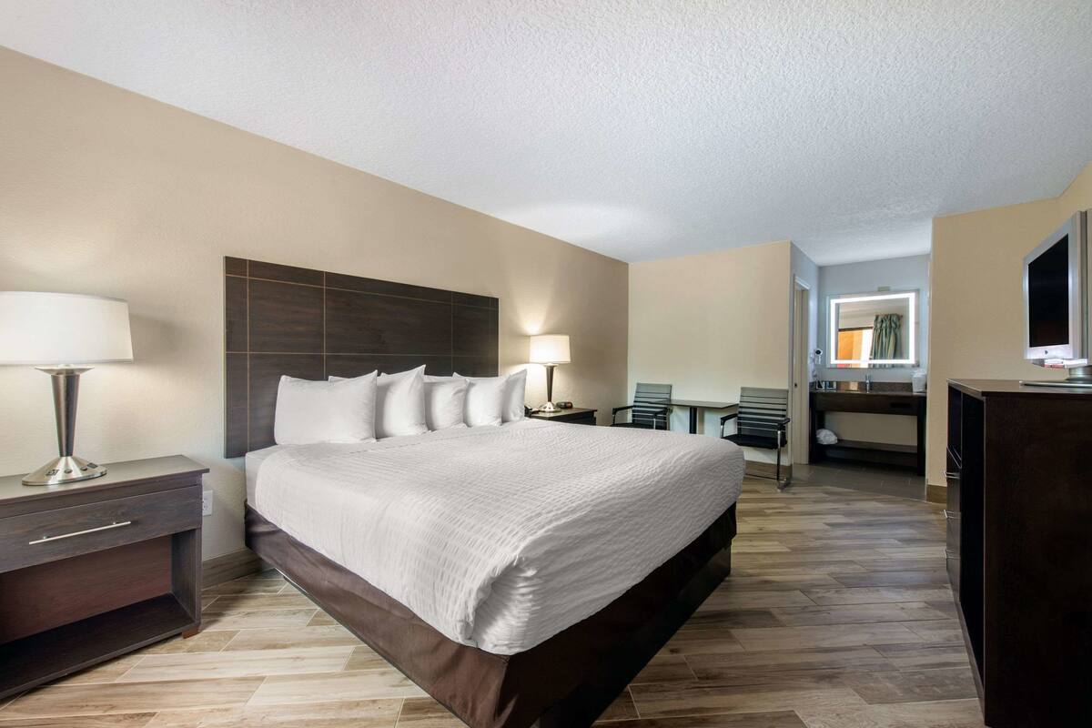 A hotel room with a large bed, bedside tables, a desk, and a mirror.