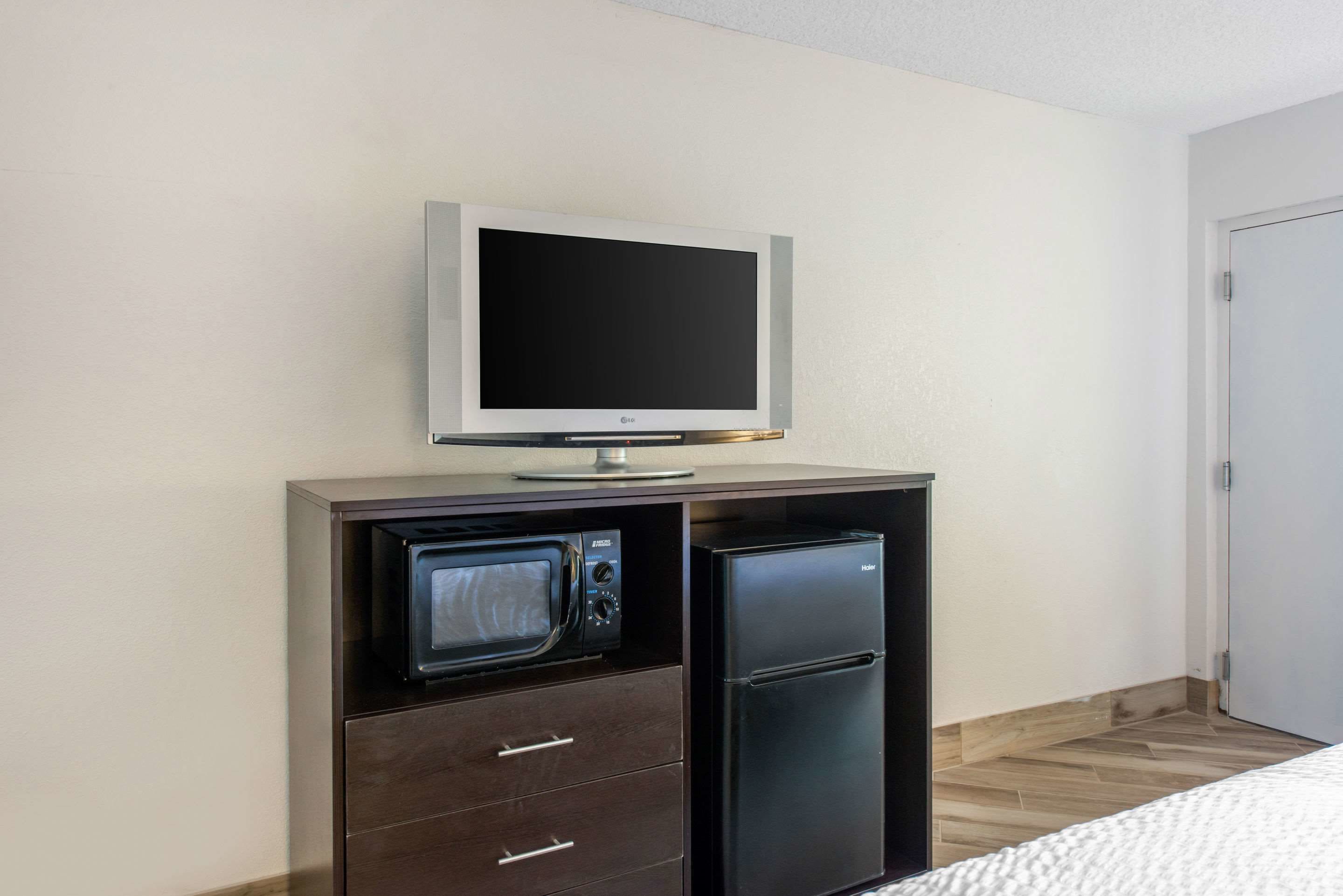 A compact kitchenette with a microwave, refrigerator, and a flat-screen TV mounted on a cabinet.