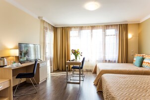 A hotel room with a desk, chair, TV, two beds, and a window with curtains.