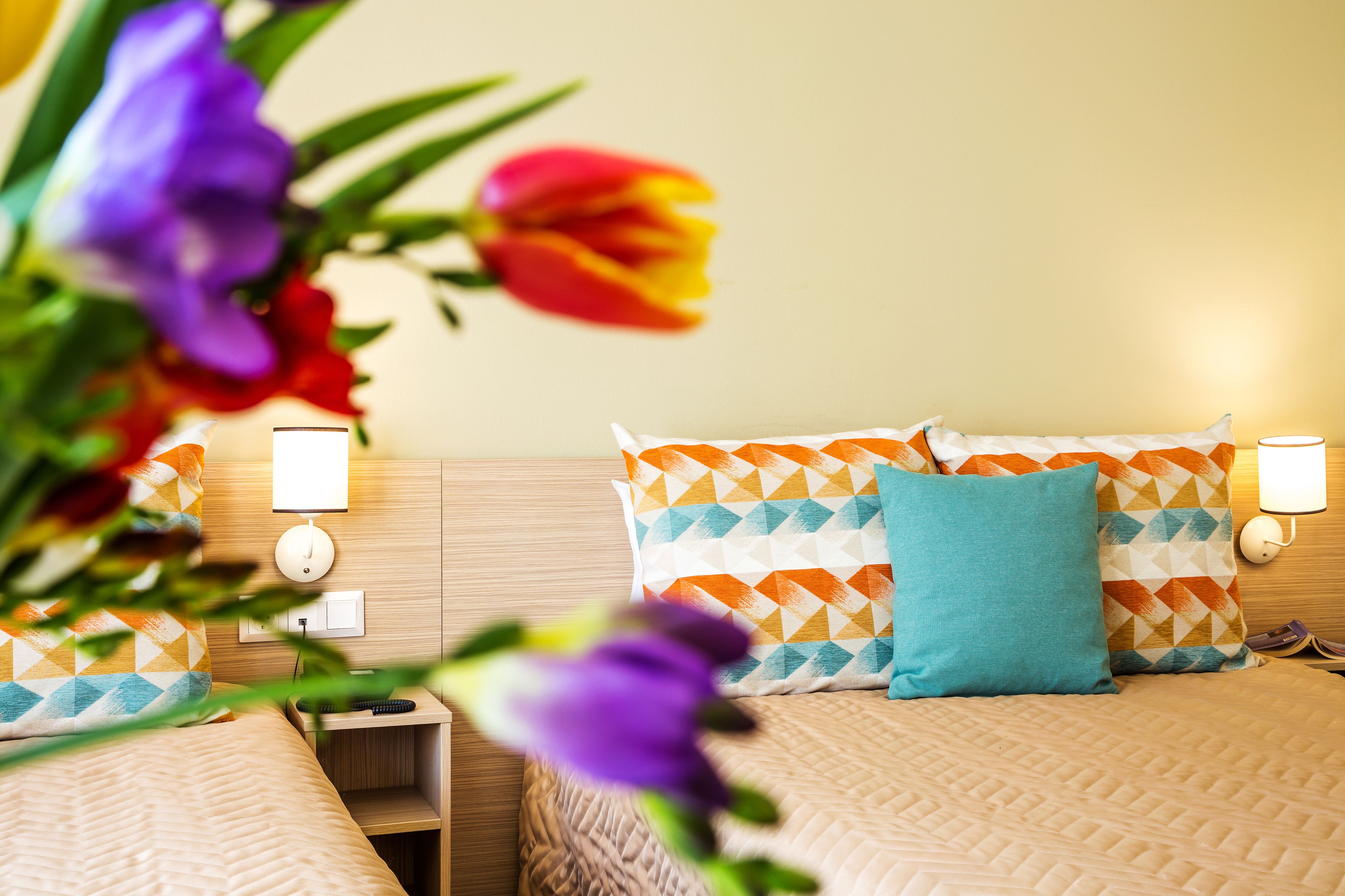 Una habitación de hotel con una cama, dos almohadas, una mesita de noche y una lámpara fijada a la pared.
