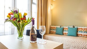 A hotel room with a bed, a bedside table with a bottle of wine and a glass, and a vase of flowers. - Hotel Geneva (Sofia)