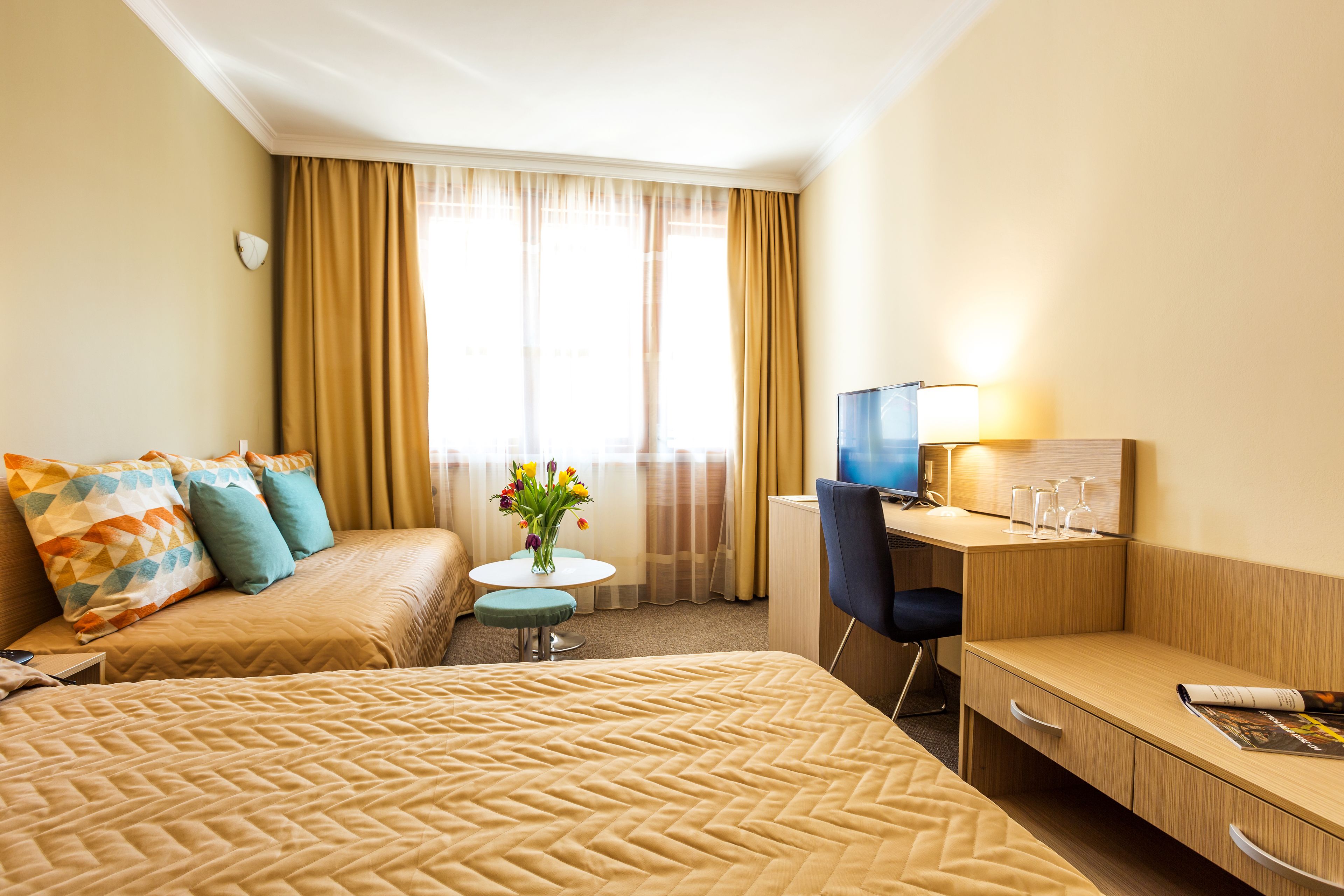 Habitación de hotel con una cama grande, un escritorio, una silla, una mesita con flores y un televisor.