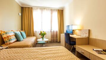 Habitación de hotel con una cama grande, un escritorio, una silla, una mesita con flores y un televisor.