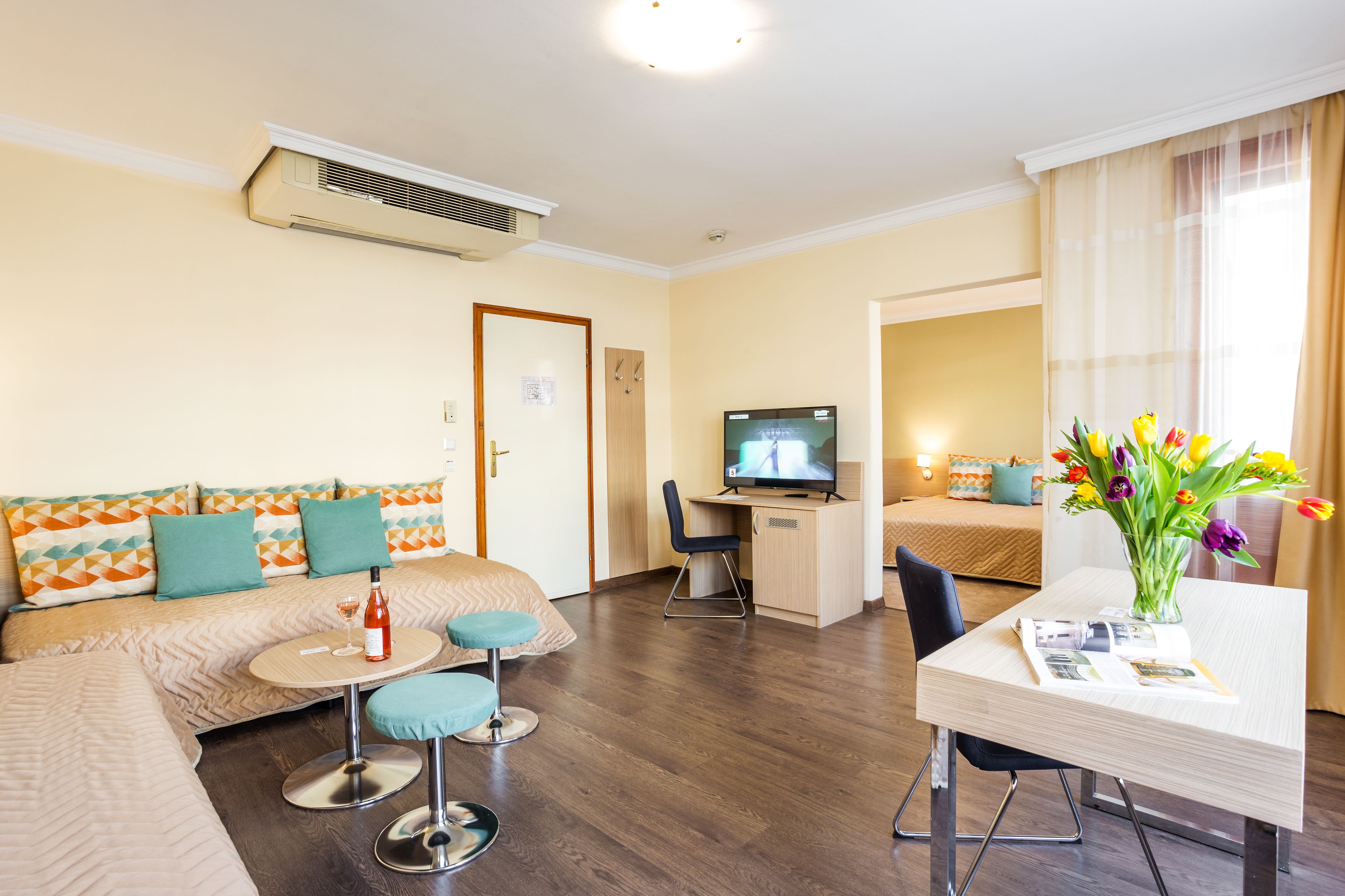 A hotel room with a sofa, a small round table, a TV, a desk, and a vase of flowers.