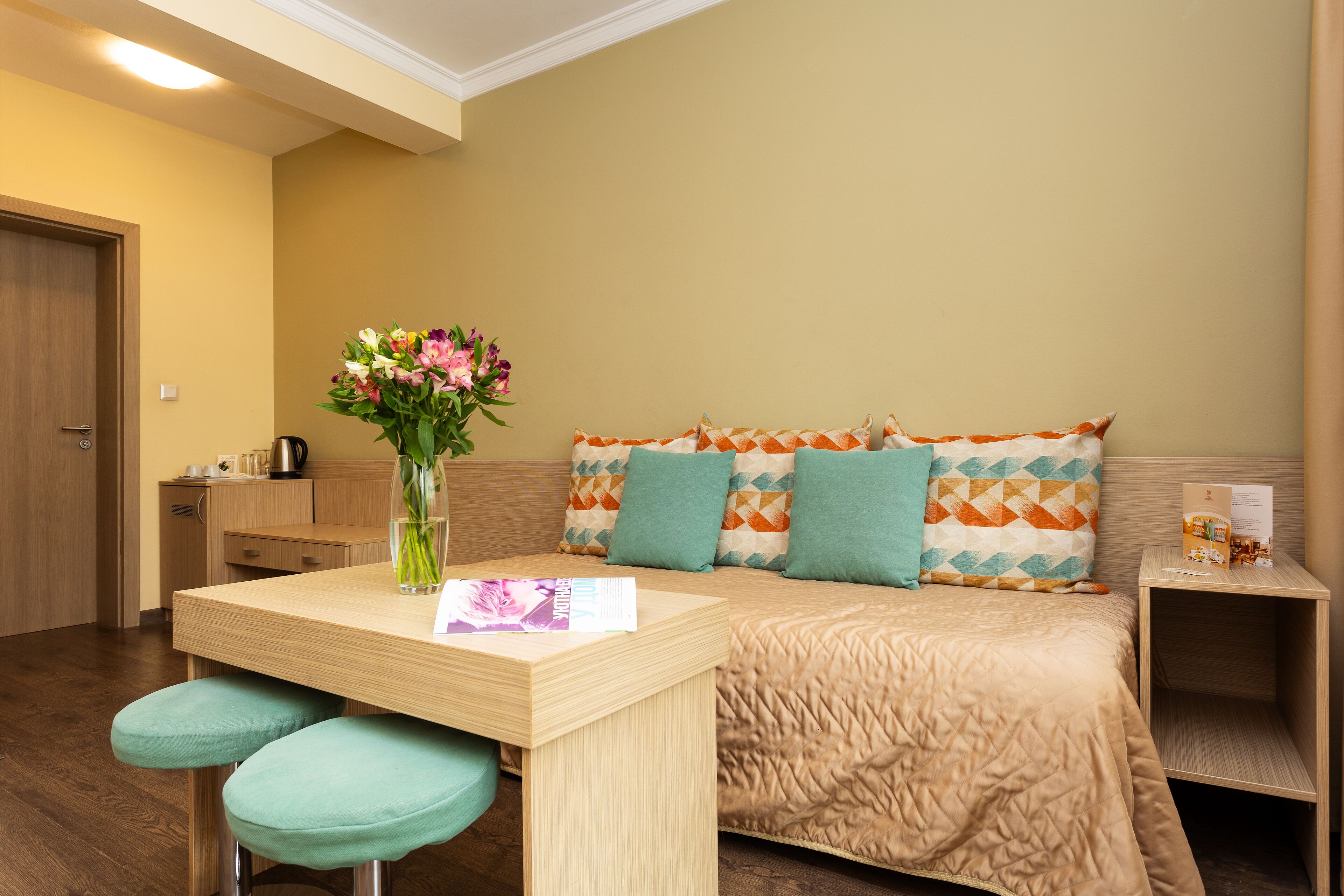 A hotel room with a bed, a table with a vase of flowers, and a small kitchenette.