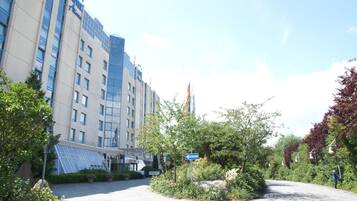 Ein Hotel mit moderner Glasfassade, einem angelegten Garten und blauem Himmel.