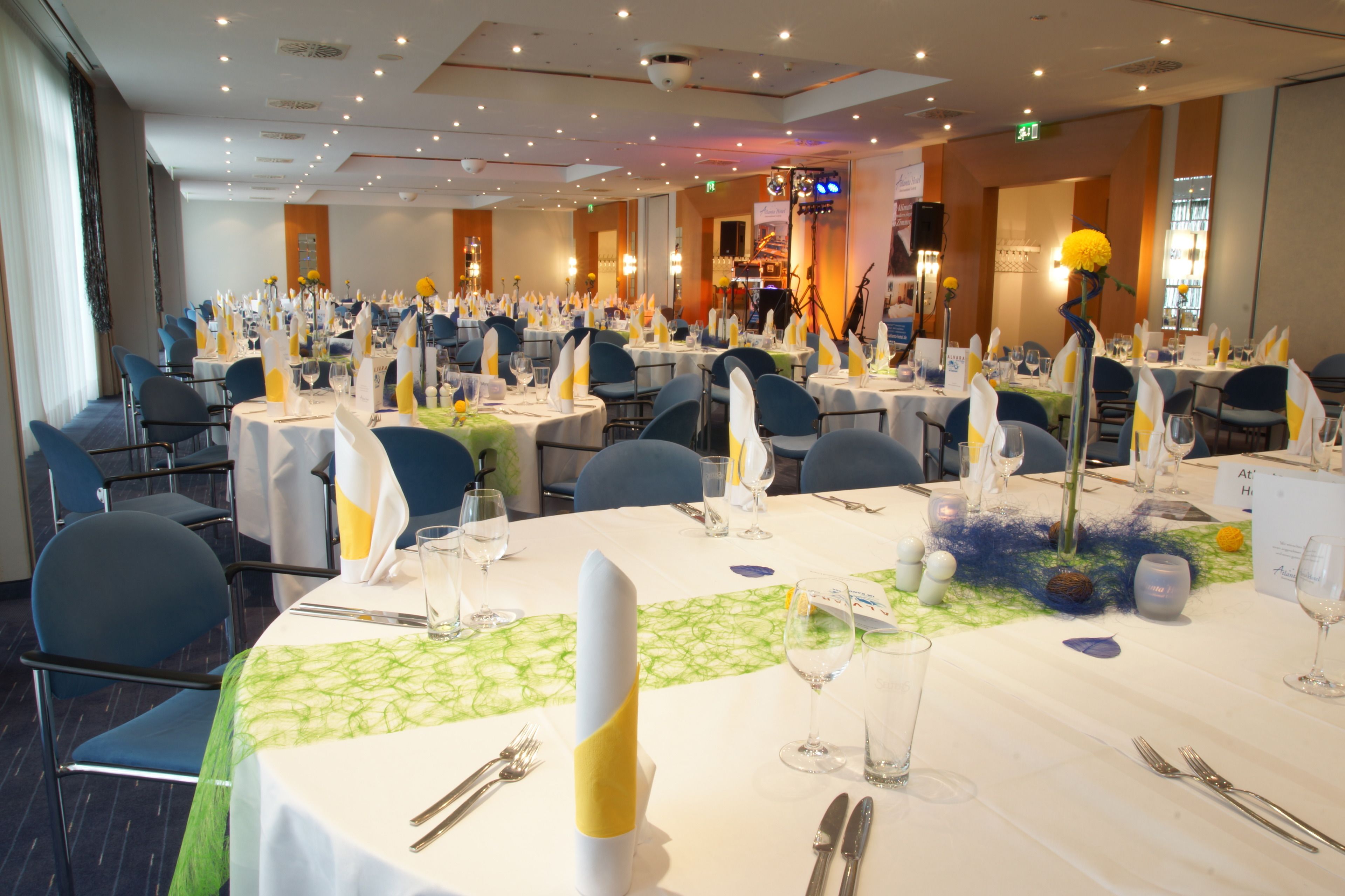 Une salle de banquet avec des tables rondes dressées pour le repas, équipées de chaises, de nappes et de centres de table.